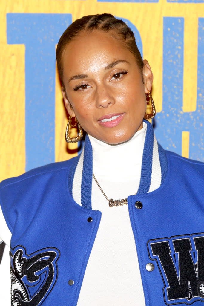 Alicia Keys wearing a blue and white varsity jacket with large letter W, hoop earrings, and a turtleneck