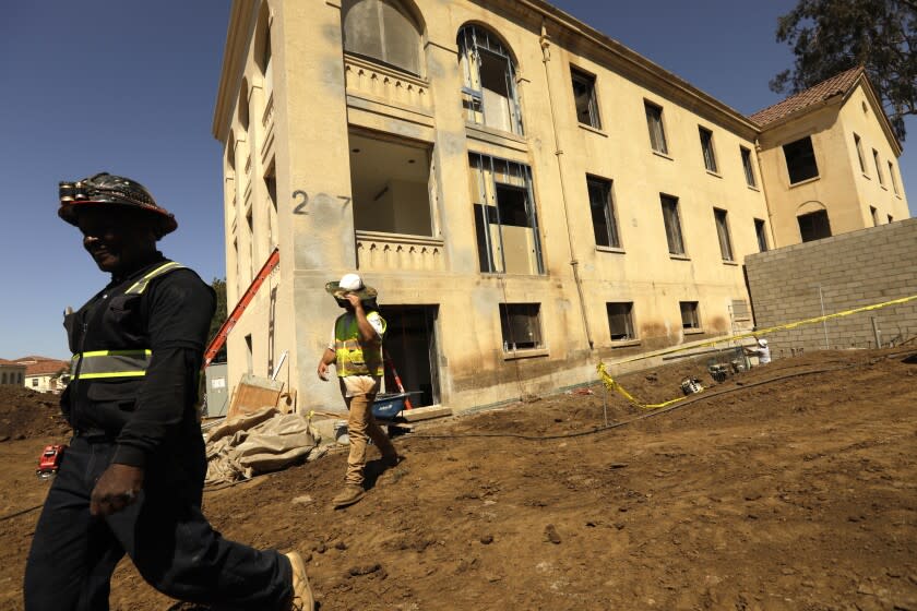 LOS ANGELES, CA - JUNE 23, 2022 - - Construction workers walk past Building 207 that is being refurbished as housing for veterans on the Veteran Affairs West LA campus in Los Angeles on June 23, 2022. This is the Collective's first project, a 60-unit building for senior veterans and their families and is scheduled to open this fall. Along with U.S. VETS, the Collective is made up of Century Housing, a nonprofit that builds and finances affordable housing, and Thomas Saffran and Associates, a Brentwood-based for-profit affordable housing developer. The master plan calls for 14 buildings to be brought up to current standards but preserved in their original form with another 14 built from the ground up. (Genaro Molina / Los Angeles Times)