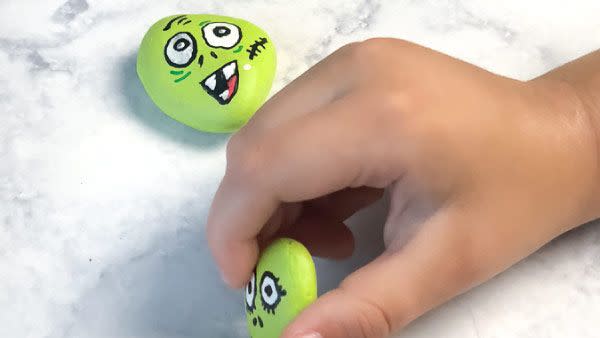 child's hands playing with rocks painted green with faces to resemble zombies