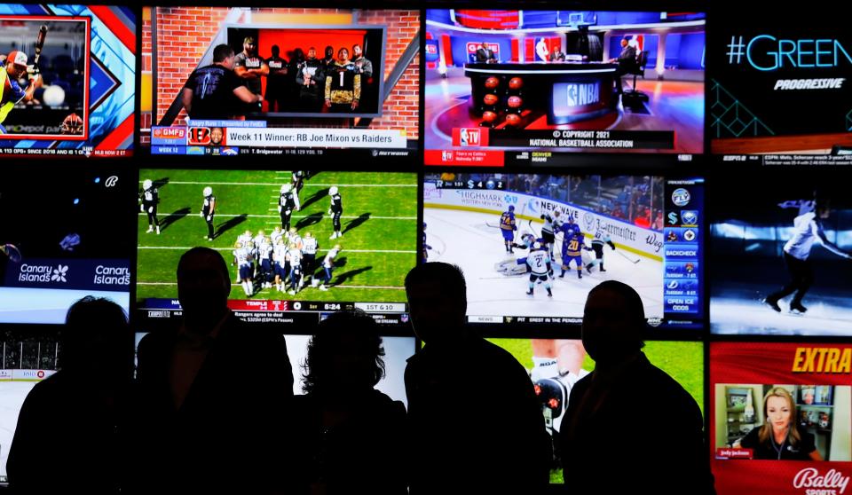 A group of people stand in front of a wall of televisions showing a variety of sports during the opening ceremony of the Oneida Casino's sports betting operation on Nov. 30, 2021, in Ashwaubenon, Wis.
