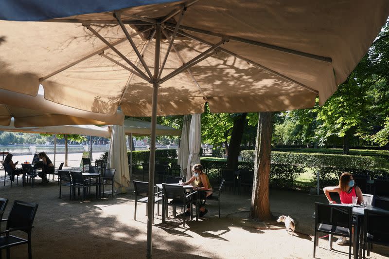 People wearing face masks sit at an outdoor seating section of a kiosk at Retiro Park as it is reopened for the first time in more than 2 months in Madrid