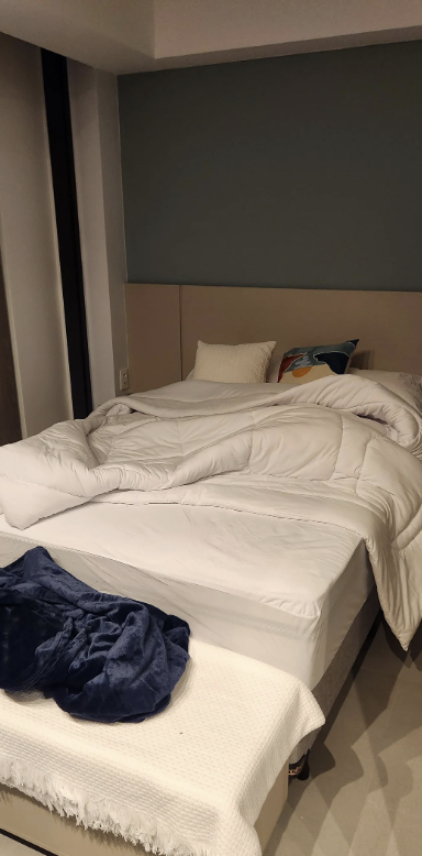 Unmade bed with white bedding and multiple pillows in a bedroom. Blue clothing item on the bed's corner