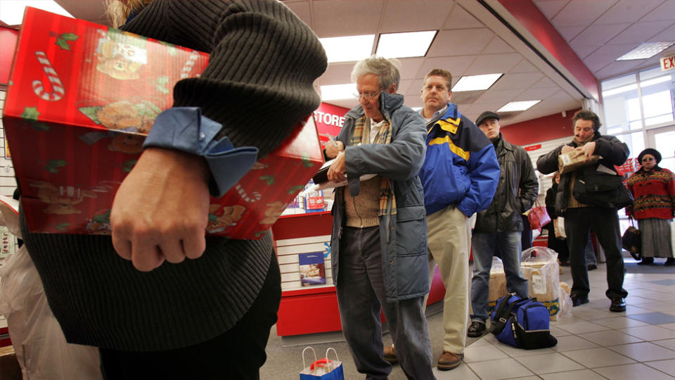 People lined up at the post office with packages and mail.