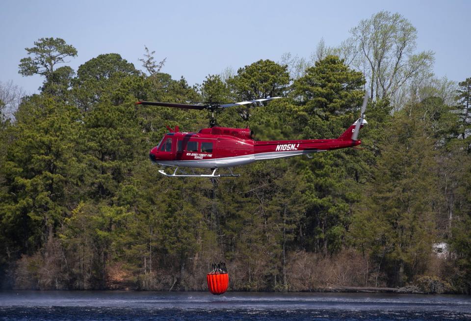 A helicopter from New Jersey State Forest Fire Service helps to fight the fire. It refills with water at Lake Horicon. First responders battle the “Jimmy’s Waterhole Fire” early in the day. The fire raged overnight threatening structures but firefighters have made progress in extinguishing the blaze.Lakehurst, NJWednesday, April 12, 2023