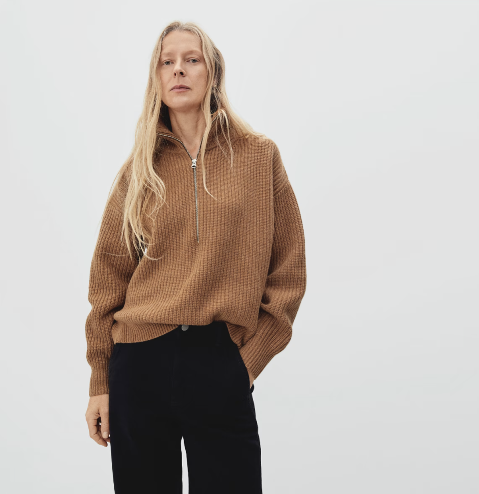 blonde woman wearing black pants and brown The Felted Merino Half-Zip Sweater in deep camel (Photo via Everlane)