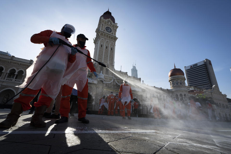 City hall workers spray a disinfectant Merdeka Square, or independence square, situated in front of the Sultan Abdul Samad Building, background, in Kuala Lumpur, Malaysia, Saturday, Oct. 17, 2020. Malaysia will restrict movements in its biggest city Kuala Lumpur, neighboring Selangor state and the administrative capital of Putrajaya from Wednesday in an attempt to curb a sharp rise in coronavirus cases. (AP Photo/Vincent Thian)