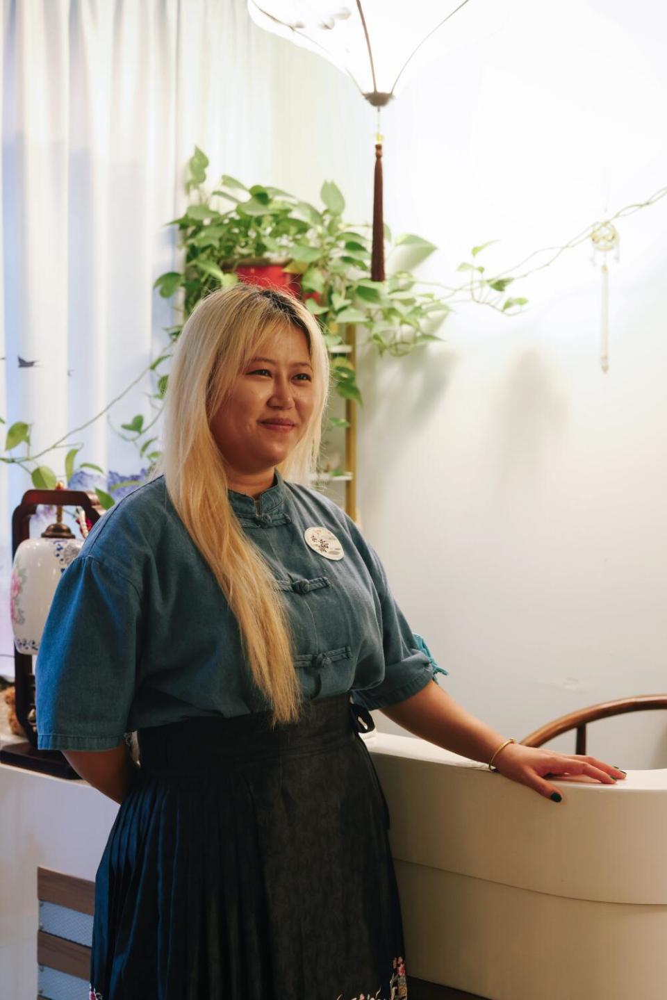 A woman with long blond hair stands at a wooden desk at a head spa.