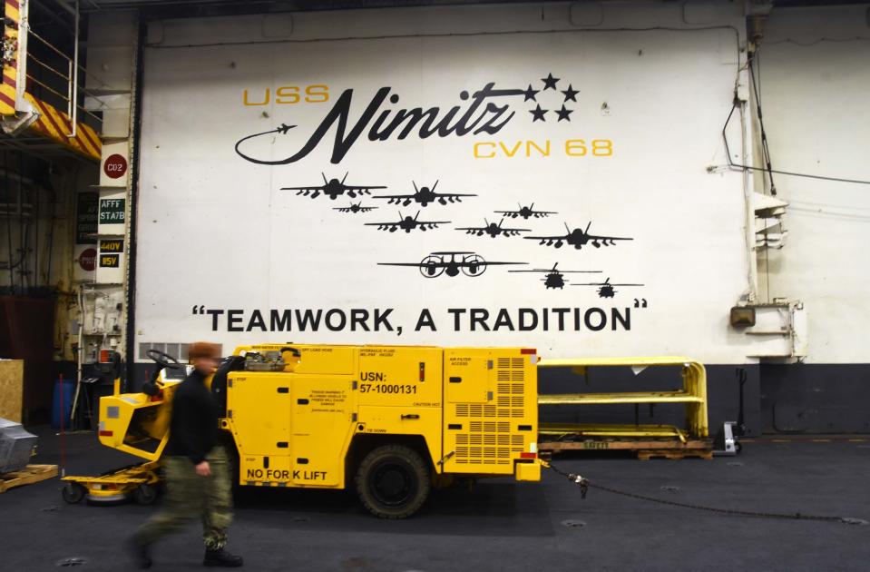 A sailor walks by a wall that painted "TEAMWORK, A TRADITION" at the Hangor Bay on the Bremerton-based aircraft carrier USS Nimitz on July 1, 2023.