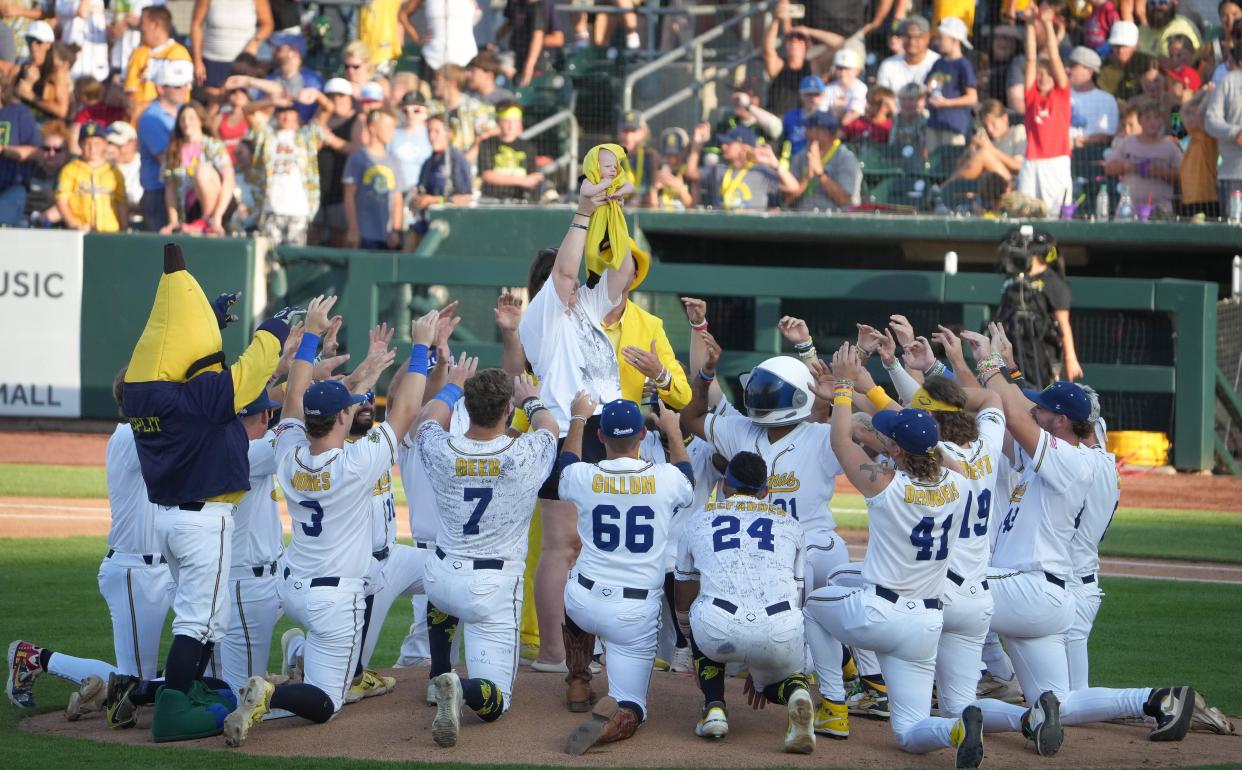 Members of the Savannah Bananas baseball team surround a young baby prior to the start of a baseball game against the Party Animals on Friday, Aug. 25, 2023, at Principal Park in Des Moines.