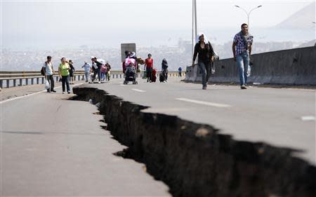 People walk next to a crack along a damaged road leading to Alto Hospicio commune, after a series of aftershocks, in the northern port of Iquique April 3, 2014. REUTERS/Ivan Alvarado