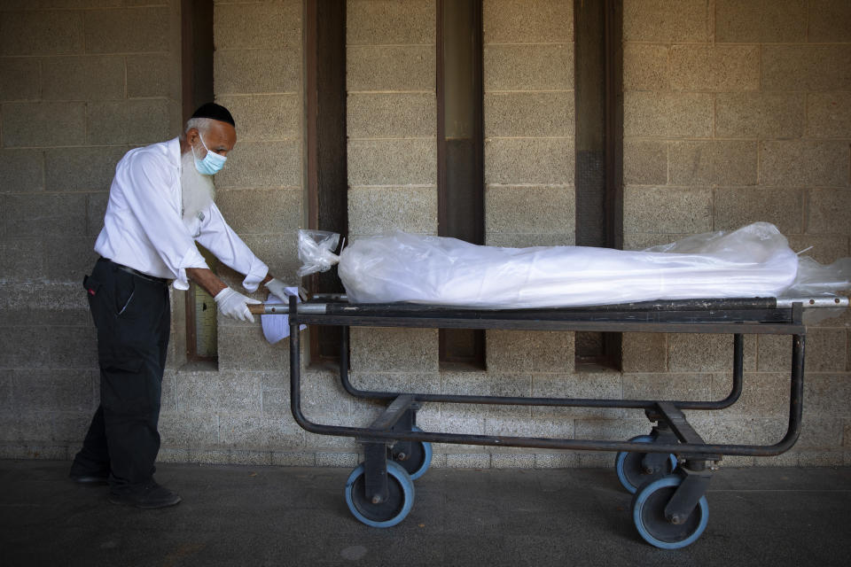 A worker from "Hevra Kadisha," Israel's official Jewish burial society, caries a body before a funeral procession at a special morgue for COVID-19 victims, during a nationwide lockdown to curb the spread of the coronavirus, in the central Israeli city of Holon, near Tel Aviv, Monday, Oct. 12, 2020. (AP Photo/Oded Balilty)