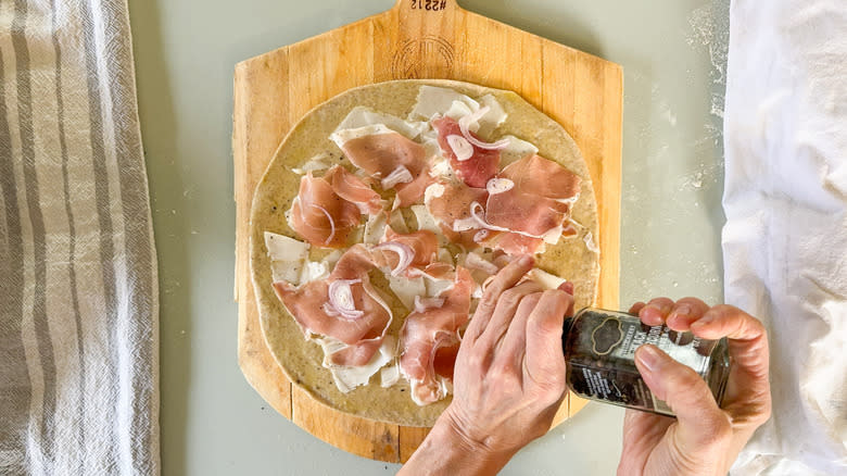 Cracking black pepper on flatbread with shaved goat gouda and torn prosciutto on pizza peel