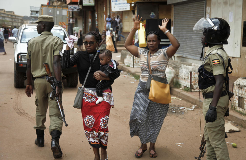 Residents walk with their hands in the air as they pass security forces pursuing protesters in Kampala, Uganda, Monday, Aug. 20, 2018. Ugandan police fired bullets and tear gas to disperse a crowd of protesters demanding the release of jailed lawmaker, pop star, and government critic Kyagulanyi Ssentamu, whose stage name is Bobi Wine. (AP Photo/Stephen Wandera)
