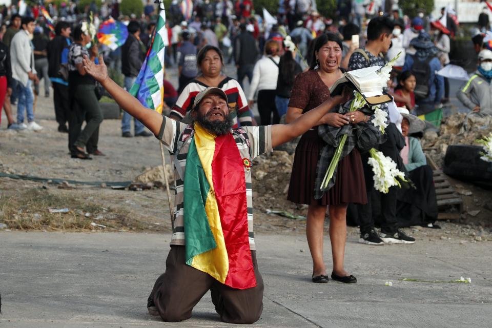 A coca leaf producer kneels holding a bible with his arms outspread asking police to open the way so a march by backers of former President Evo Morales may continue to Cochabamba, Bolivia, Nov. 16, 2019. (AP Photo/Juan Karita)