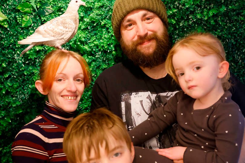 The family pose in front of a green background with Flori to the left perched on Lucie's head
