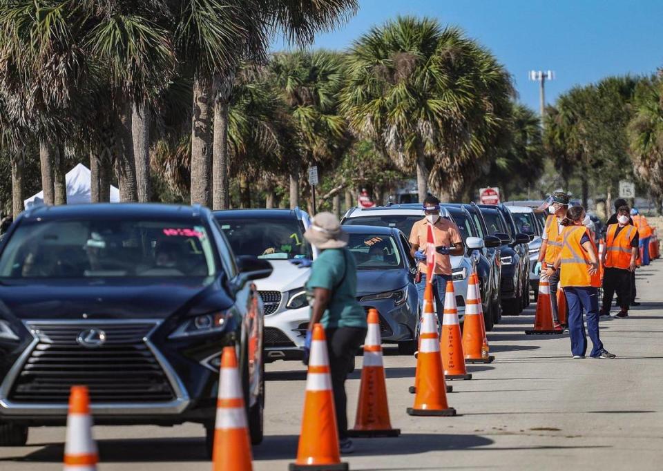 On Sunday, January 3, 2021 motorists line-up for COVID-19 vaccination shots for people who are 65 and older as site staffers assist at Vista View Park in Davie, Florida.