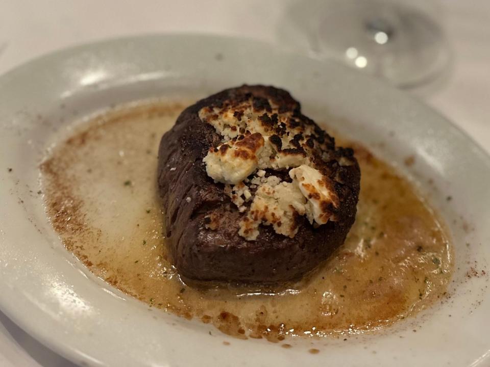 steak with blue cheese on top in a pool of butter on a plate next to glass of red wine