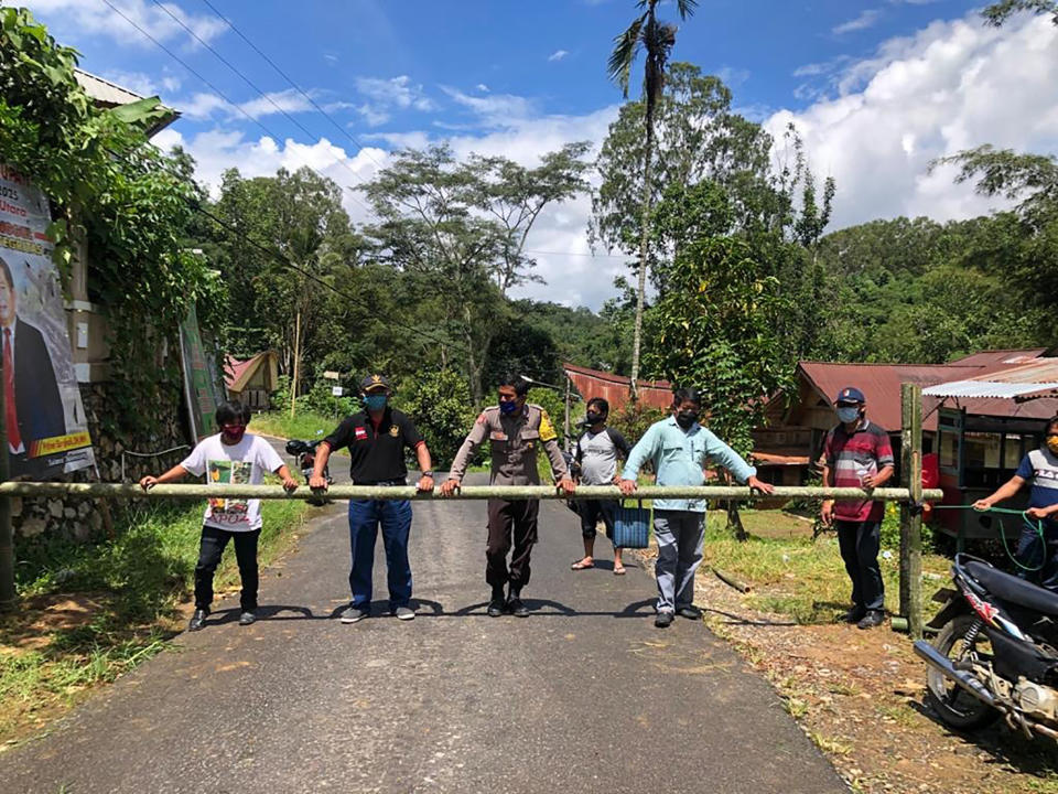 In this April 24, 2020, photo, provided by the Indigenous People Alliance of the Archipelago, indigenous peoples from the Buntao’ community in Indonesia’s North Toraja regency in South Sulawesi Province use a wooden barrier to block off their village. Indigenous peoples across the archipelago are locking down their villages in an effort to protect their communities from the coronavirus. (AMAN via AP)