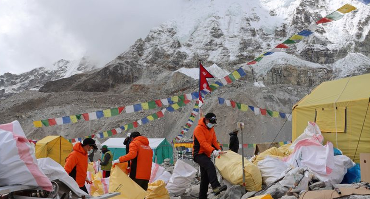 Three men hold plastic bags cleaning up with the high peak of Mount Everest behind them.