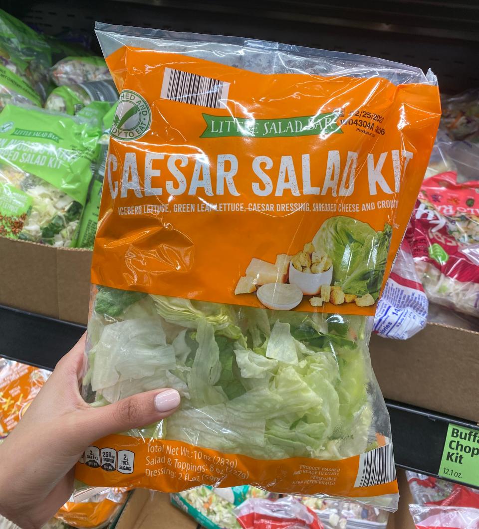 Hand holding orange and clear bag of caesar salad kit at Aldi