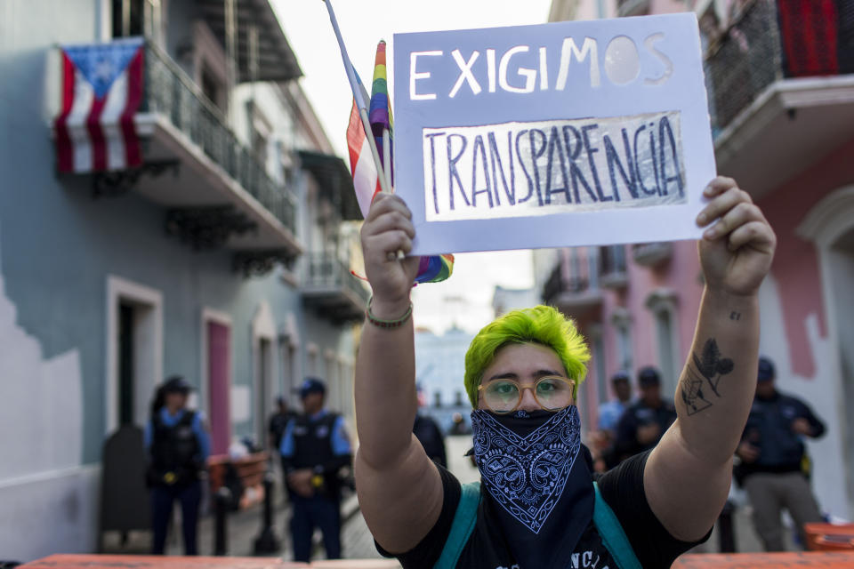 A demonstrator holds up a sign with a message that reads in Spanish: "We demand transparency" outside the government mansion La Fortaleza, where a small group of protesters gathered, in San Juan Puerto Rico, Friday, Aug. 9, 2019. The protests that led to the resignation of Gov. Ricardo Rossello on Aug. 2 and continued on a smaller scale until the Supreme Court removed his chosen successor are dissipating. (AP Photo/Dennis M. Rivera Pichardo)