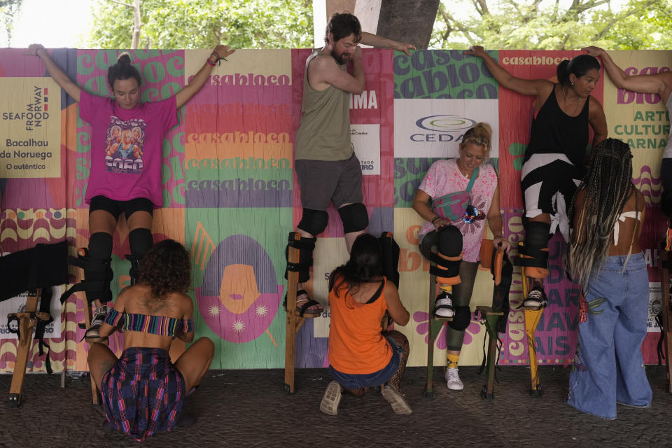 Volunteering former students, and instructor Raquel Potí, far right, help workshop participants strap on wooden stilts, at the Museum of Modern Art in Rio de Janeiro, Brazil, Saturday, Jan. 27, 2024. Potí’s workshop has a five-person production team, with planning meetings for communications and sales. (AP Photo/Silvia Izquierdo)