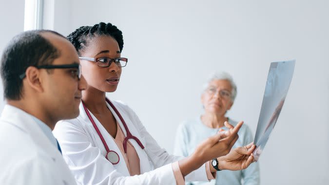 Two doctors holding and looking at an x-ray in front of a senior female patient.