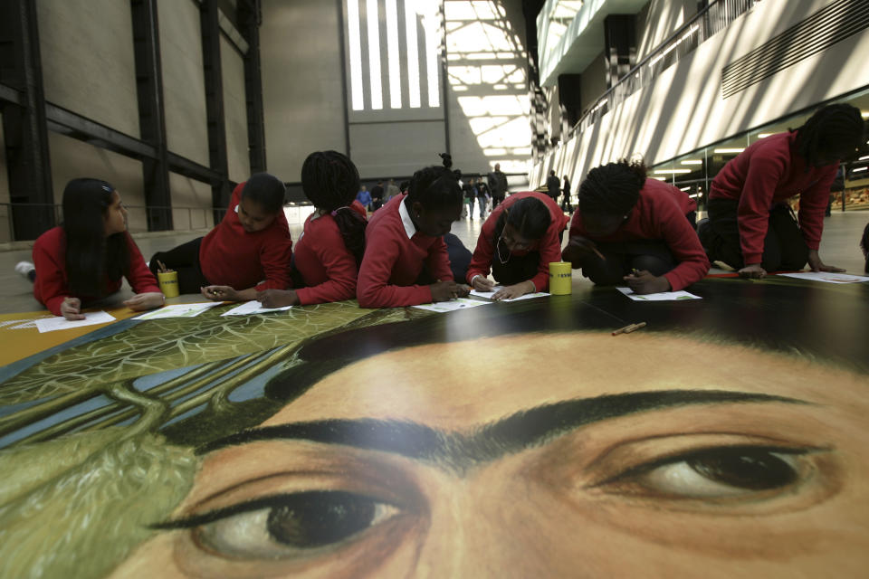 ARCHIVO - Niños colorean un cartel gigante de la artista mexicana Frida Kahlo, durante una ceremonia que marca el quinto aniversario de la galería Tate Modern en Southwark, Londres, el 12 de mayo de 2005. El 70 aniversario de la muerte de Kahlo es el 13 de julio de 2024. (AP Foto/Lefteris Pitarakis, Archivo)