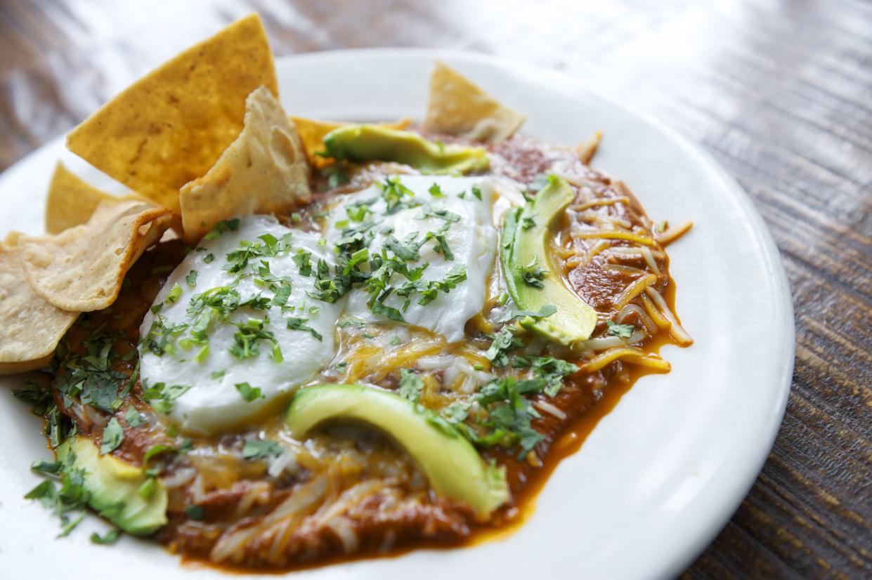 Fresh made Mexican Californian style plate of huevos rancheros ranch style poached eggs with cheese and avocado on red sauce with tortilla chips