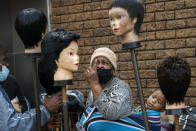 FILE - In this Sept. 16, 2020 file photo, a woman carrying a child on her back looks at wigs on sale at the Baragwanath Taxi Rank in Soweto, South Africa. The country's success in bringing its first wave of COVID-19 under control has allowed it to almost fully reopen the economy, while monitoring for signs of a second surge, says the government's chief medical advisor. (AP Photo/Jerome Delay, file)