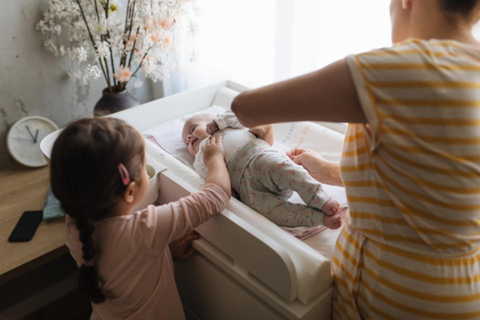 A young girl is helping her mom changing a baby