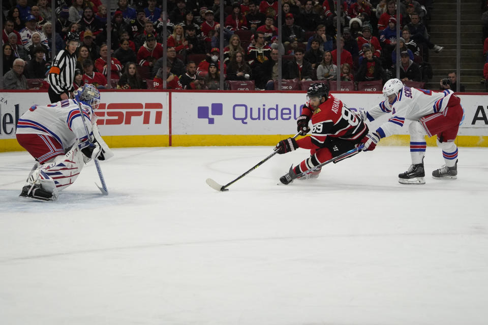 New York Rangers defenseman Braden Schneider, right, defends Chicago Blackhawks center Andreas Athanasiou (89) who skates in against Rangers goaltender Igor Shesterkin (31) during the first period of an NHL hockey game Sunday, Dec. 18, 2022, in Chicago. (AP Photo/David Banks)