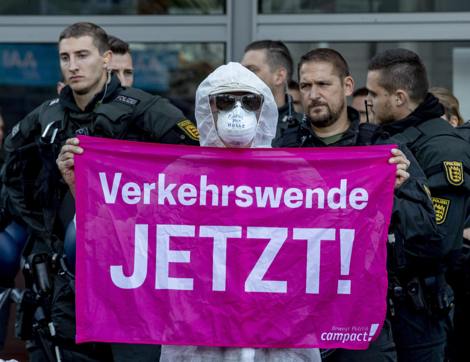 An activist holds a banner reading "traffic change now" as he blocks the main entrance of the fairground in Frankfurt, Germany, Sunday, Sept. 15, 2019. They protest against the government's transport policy on occasion of the IIA Auto Show taking place. The slogan on the face mask reads : 'Drive to hell'. (AP Photo/Michael Probst)