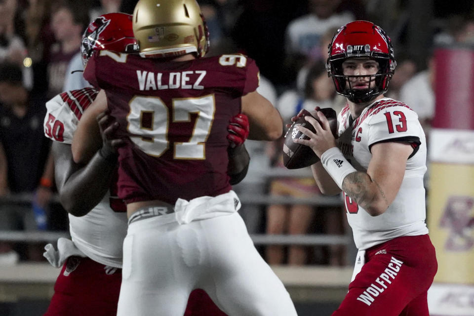 North Carolina State quarterback Devin Leary (13) drops back to pass as teammate Grant Gibson(50) blocks Boston College defensive end Marcus Valdez (97) during the first half of an NCAA college football game, Saturday, Oct. 16, 2021, in Boston. (AP Photo/Mary Schwalm)