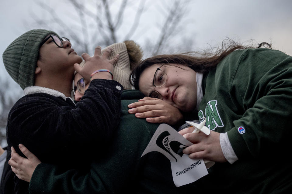 Michigan State seniors Aaron Iturralde, from left to right, Ellie Bennett and Carla Coleman find solace in each other's embrace on Wednesday, Feb. 15, 2023, at The Rock, a popular college landmark at Michigan State University, where a makeshift memorial continues to grow with flowers and keepsakes following Monday's shootings on the campus in East Lansing, Mich. (Jake May/The Flint Journal via AP)