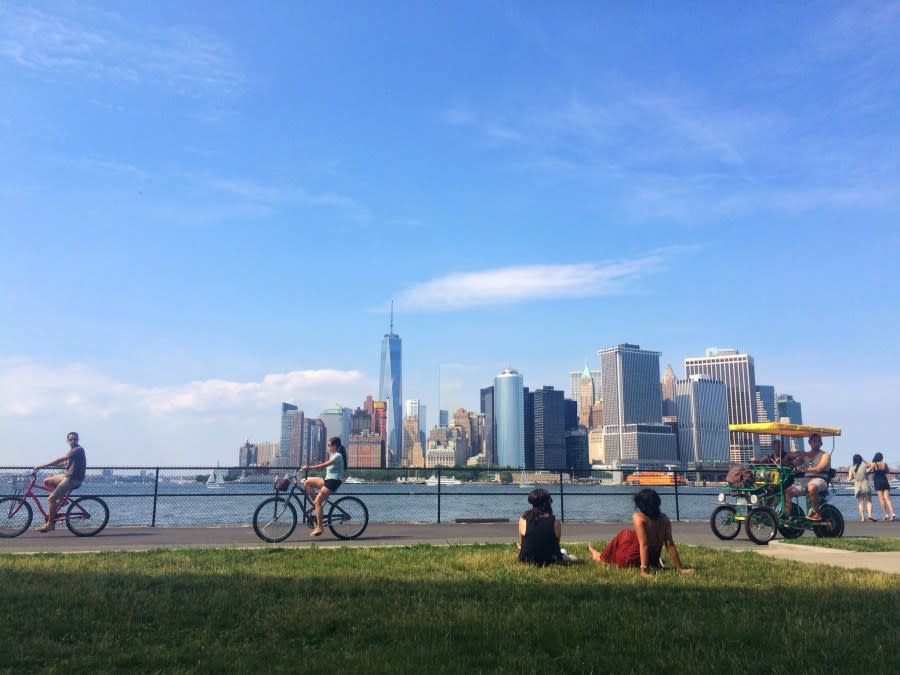 People enjoying a summer day on Governors Island looking out at the Manhattan skyline. (Credit: Stacey Bramhall / Getty Images)