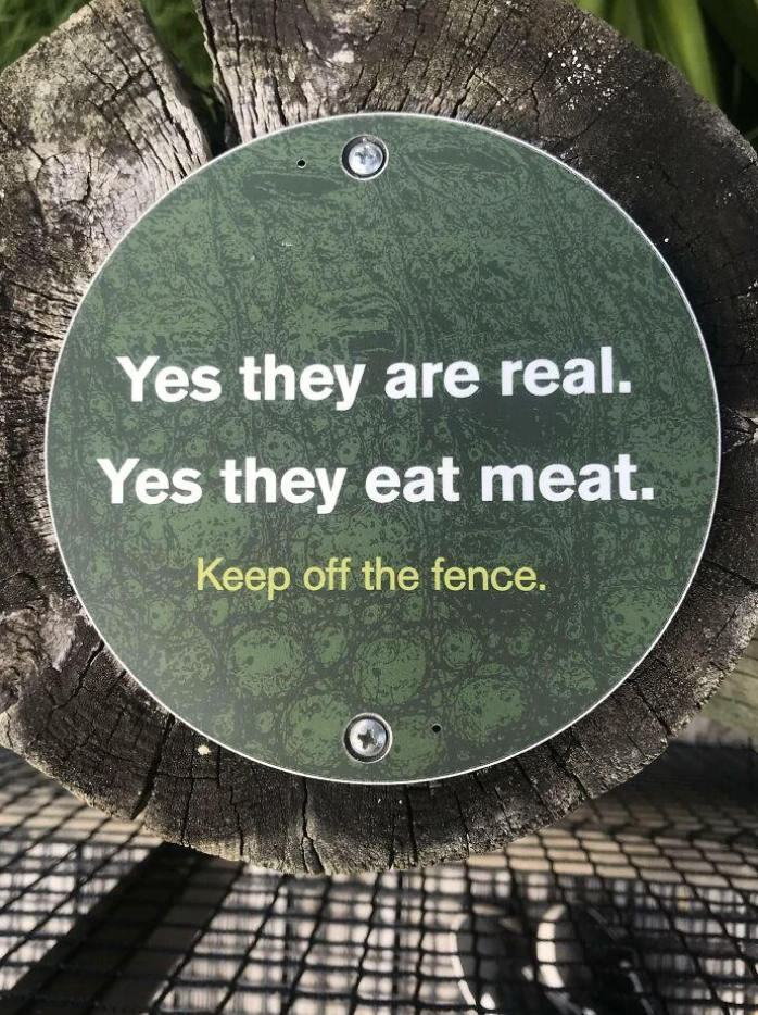 Sign on a fence warning: "Yes they are real. Yes they eat meat. Keep off the fence."