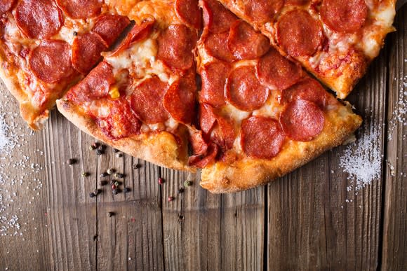 Slices of a pepperoni pizza on a wood table.