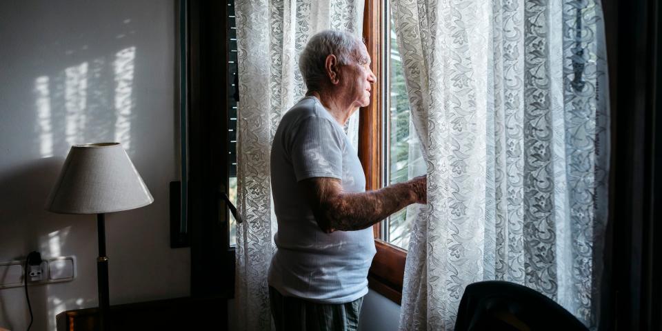 sad older man looking through the window in retirement