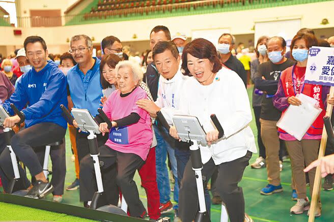 嘉義市8日在港坪體育館辦理「i嘉科技運動會」，市長黃敏惠（前排右）與90歲阿嬤薛鄭鶴（粉紅衣者）比賽「智慧電刷車舟」軋身手，場面溫馨有趣。（廖素慧攝）