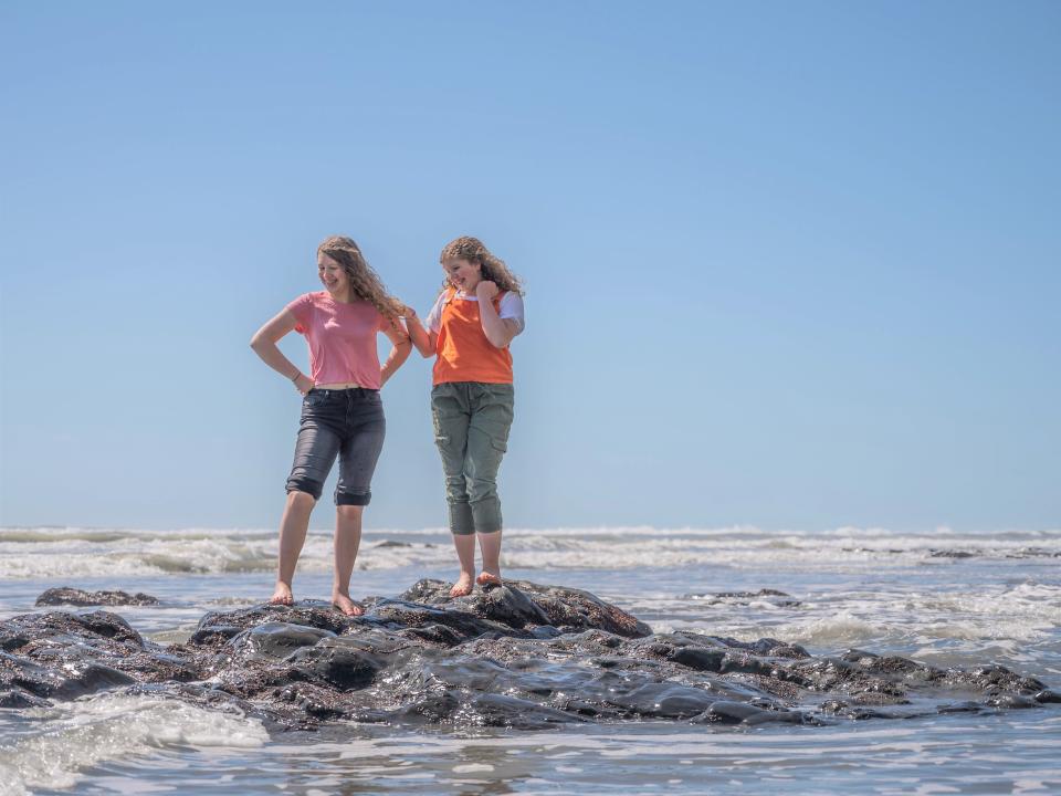 Two girls standing on a rock amid shallow water.