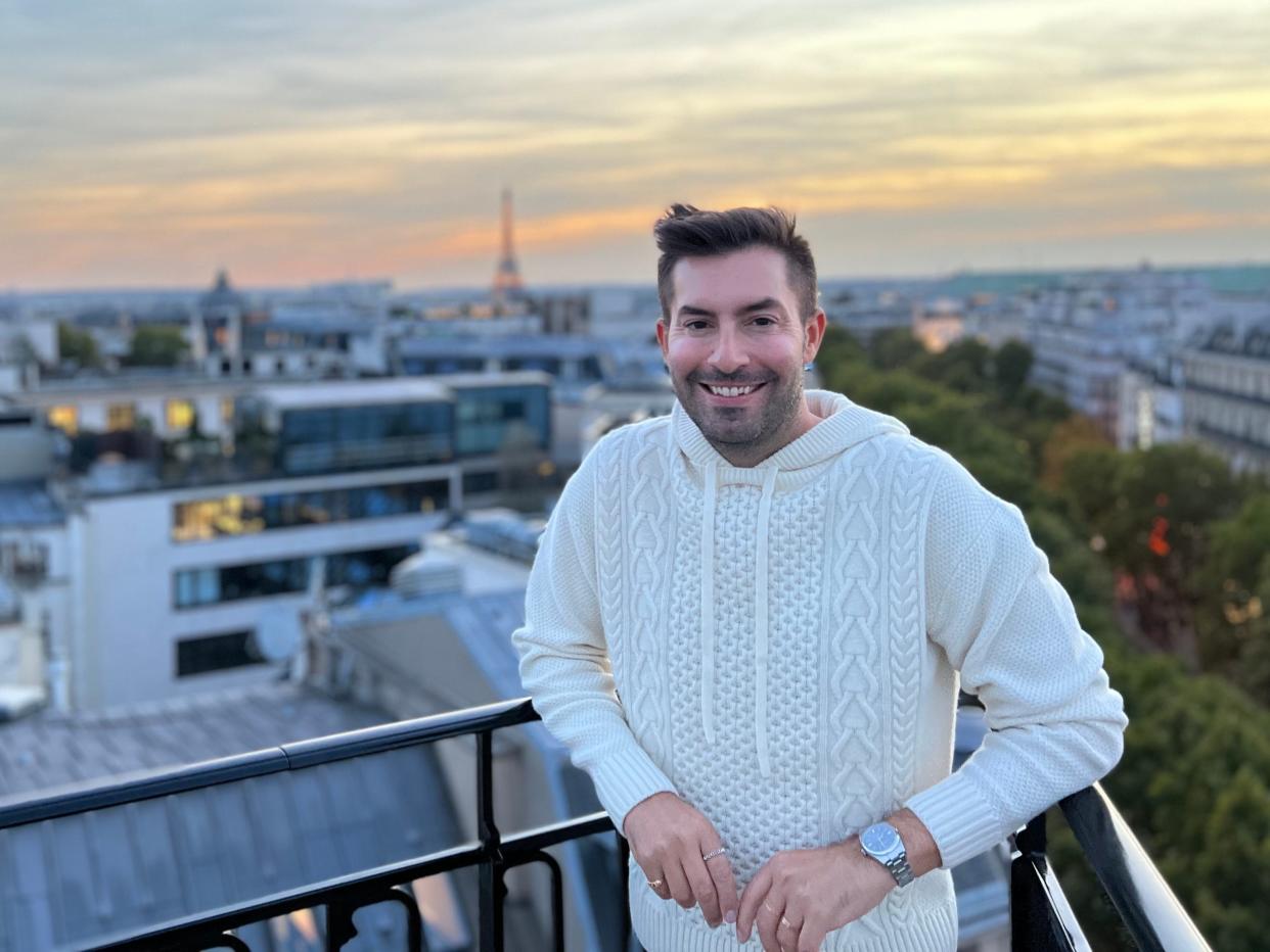 A man standing on a balcony with a view of the Eiffel Tower in the background.