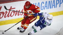 Vancouver Canucks' Nils Hoglander, right, checks Calgary Flames' Rasmus Andersson during second-period NHL hockey game action in Calgary, Alberta, Monday, Jan. 18, 2021. (Jeff McIntosh/The Canadian Press via AP)