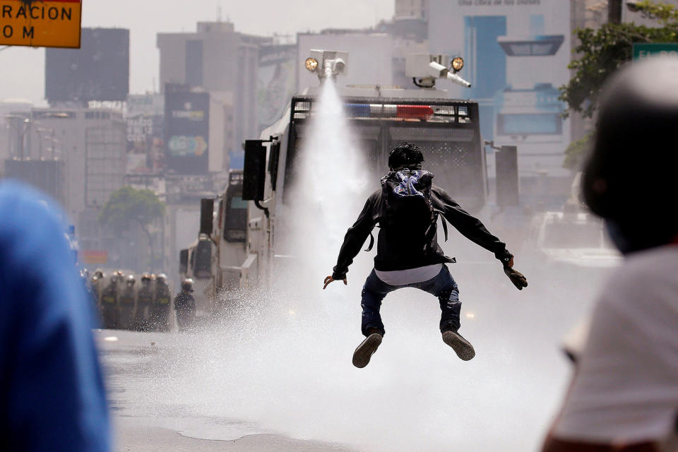 A demonstrator jumps away from a jet of water released from a riot security forces vehicle