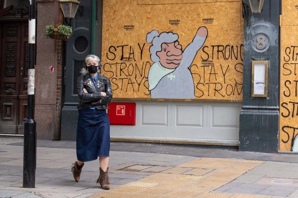 A woman wearing a protective face mask passes a boarded up pub: PA