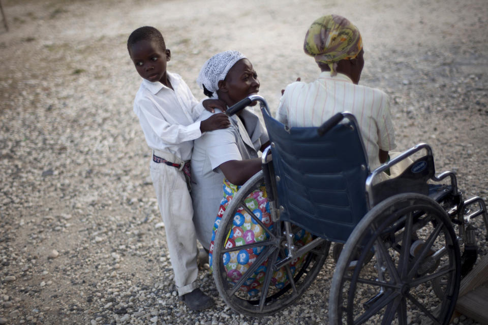In this picture taken on Feb. 12, 2012, a boy stands next to his mother as she visits with a neighbor sitting in a wheelchair at La Piste camp in Port-au-Prince, Haiti. While more than a million people displaced by the 2010 quake ended up in post-apocalyptic-like tent cities, some of the homeless disabled population landed in the near-model community of La Piste, a settlement of plywood shelters along tidy gravel lanes. However, the rare respite for the estimated 500-plus people living at the camp is coming to an end as the government moves to reclaim the land. (AP Photo/Ramon Espinosa)