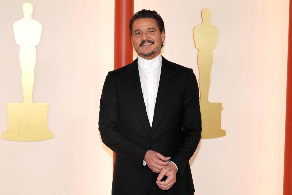 pedro pascal smiling at the camera, wearing a suit on the red carpet for the 95th annual academy awards