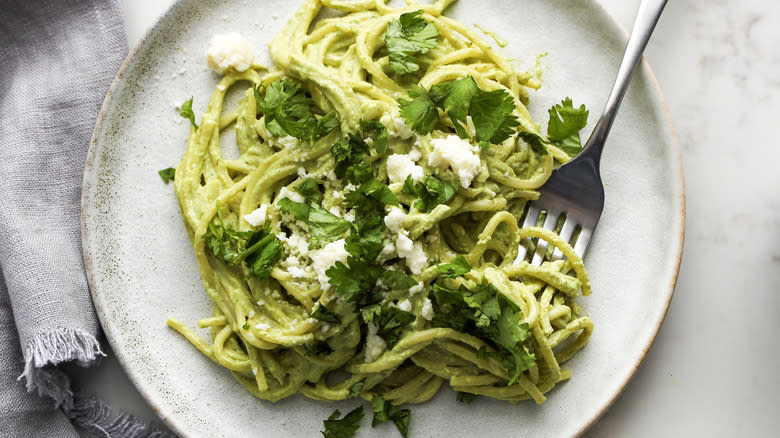 spaghetti with green sauce on ceramic plate with fork