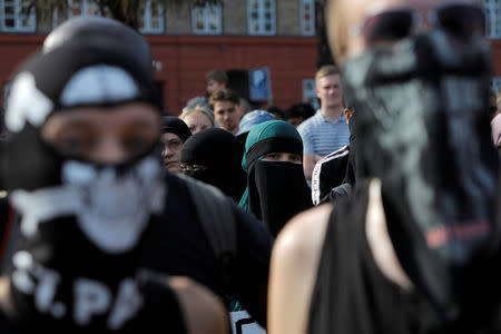 A woman in a niqab stands amongst masked protesters in a demonstration against the Danish face veil ban in Copenhagen, Denmark, August 1, 2018. REUTERS/Andrew Kelly