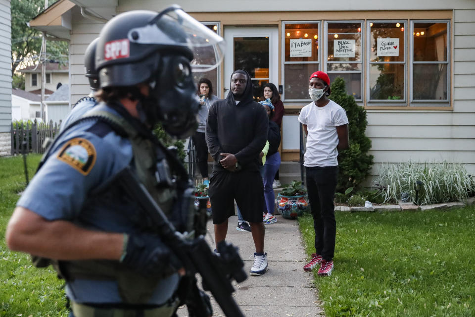 Protestors watch as police in riot gear walk down a residential street, Thursday, May 28, 2020, in St. Paul, Minn. Protests over the death of George Floyd, a black man who died in police custody Monday, broke out in Minneapolis for a third straight night. (AP Photo/John Minchillo)